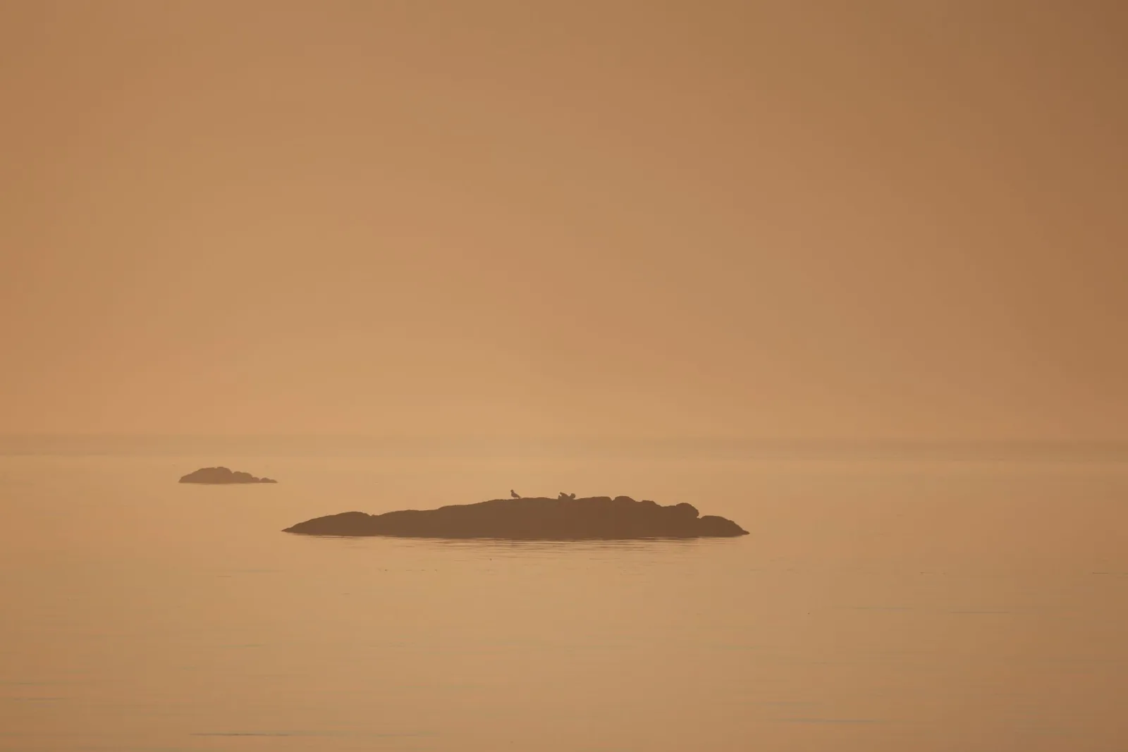 Mer et îlots sous un ciel orangé chargé de poussière en suspension, comme lors d'un épisode de calima