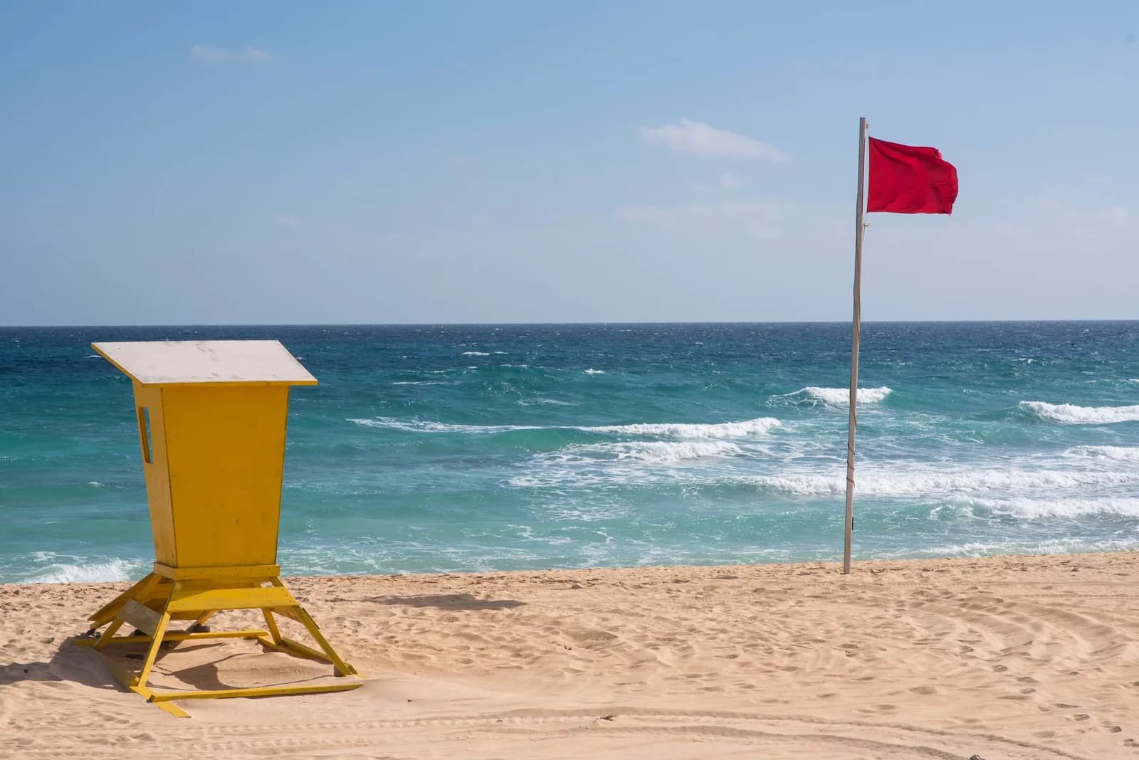 Drapeau rouge et poste de secours jaune sur une plage de sable face à l'Atlantique, îles Canaries