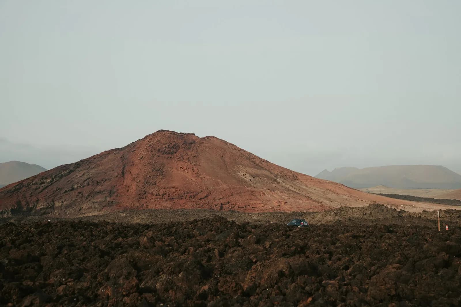 Cône volcanique rouge émergeant d'un champ de lave noire dans la région de Timanfaya, Lanzarote