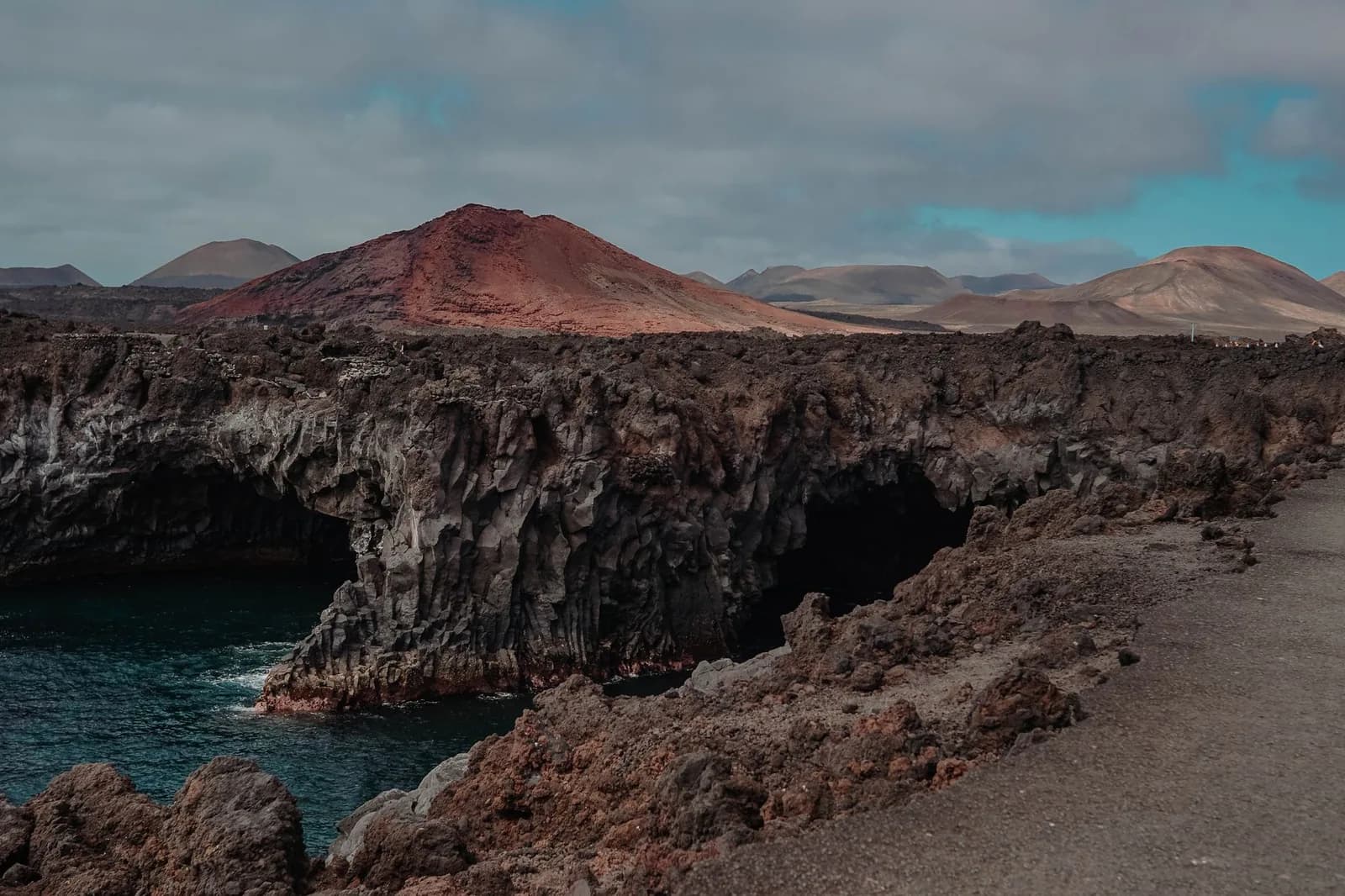 Falaises de lave noire de Los Hervideros et cône rouge de Montaña Bermeja au-dessus de l'océan, sur la côte ouest de Lanzarote