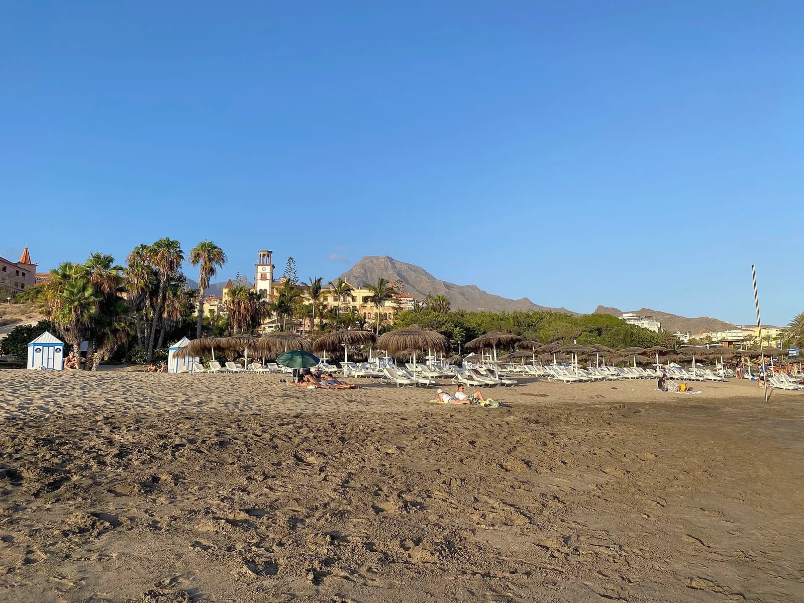 Playa del Duque à Costa Adeje, Tenerife : sable doré, cabines de plage, parasols en paille et hôtels dans les palmiers