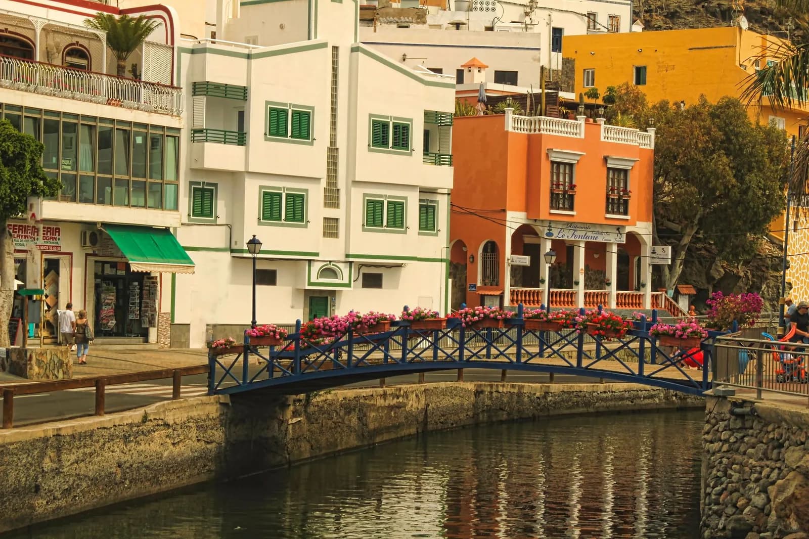 Passerelle bleue fleurie enjambant un canal entre les maisons de Puerto de Mogán, Gran Canaria