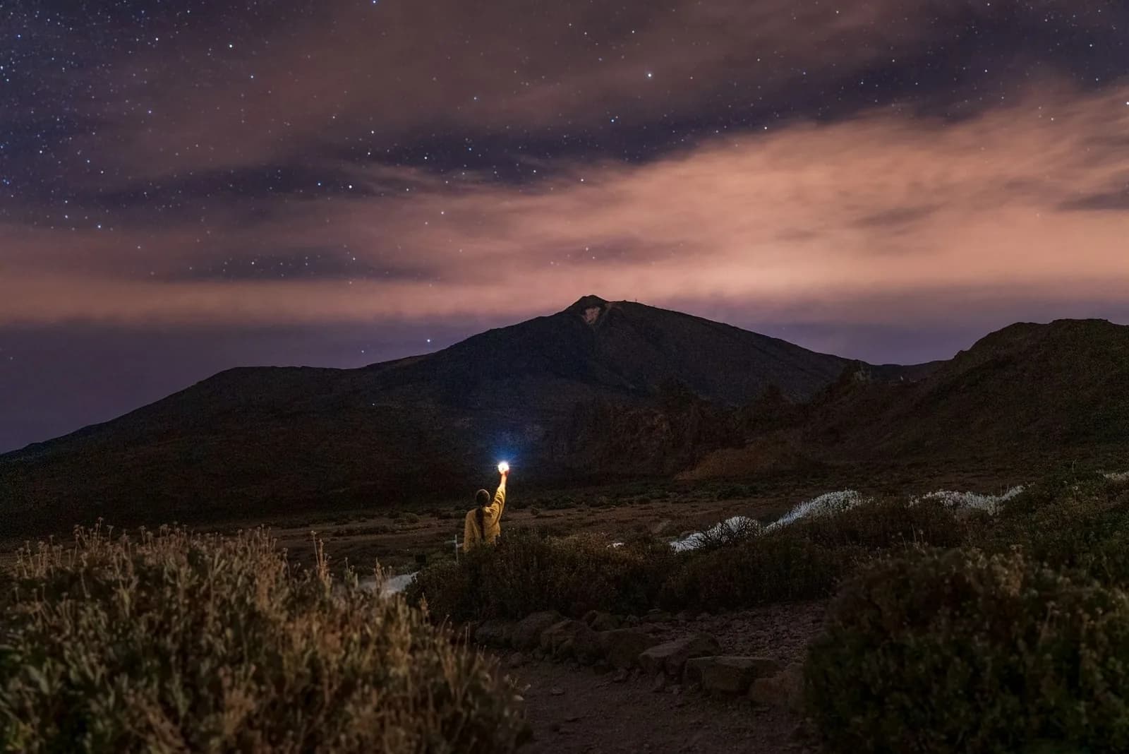 Silhouette du Teide sous un ciel étoilé, un marcheur tenant une lampe frontale au premier plan, parc national du Teide