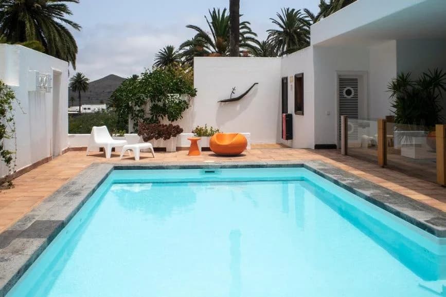 Villa blanche avec piscine et terrasse entourée de palmiers, un volcan en arrière-plan, à Lanzarote