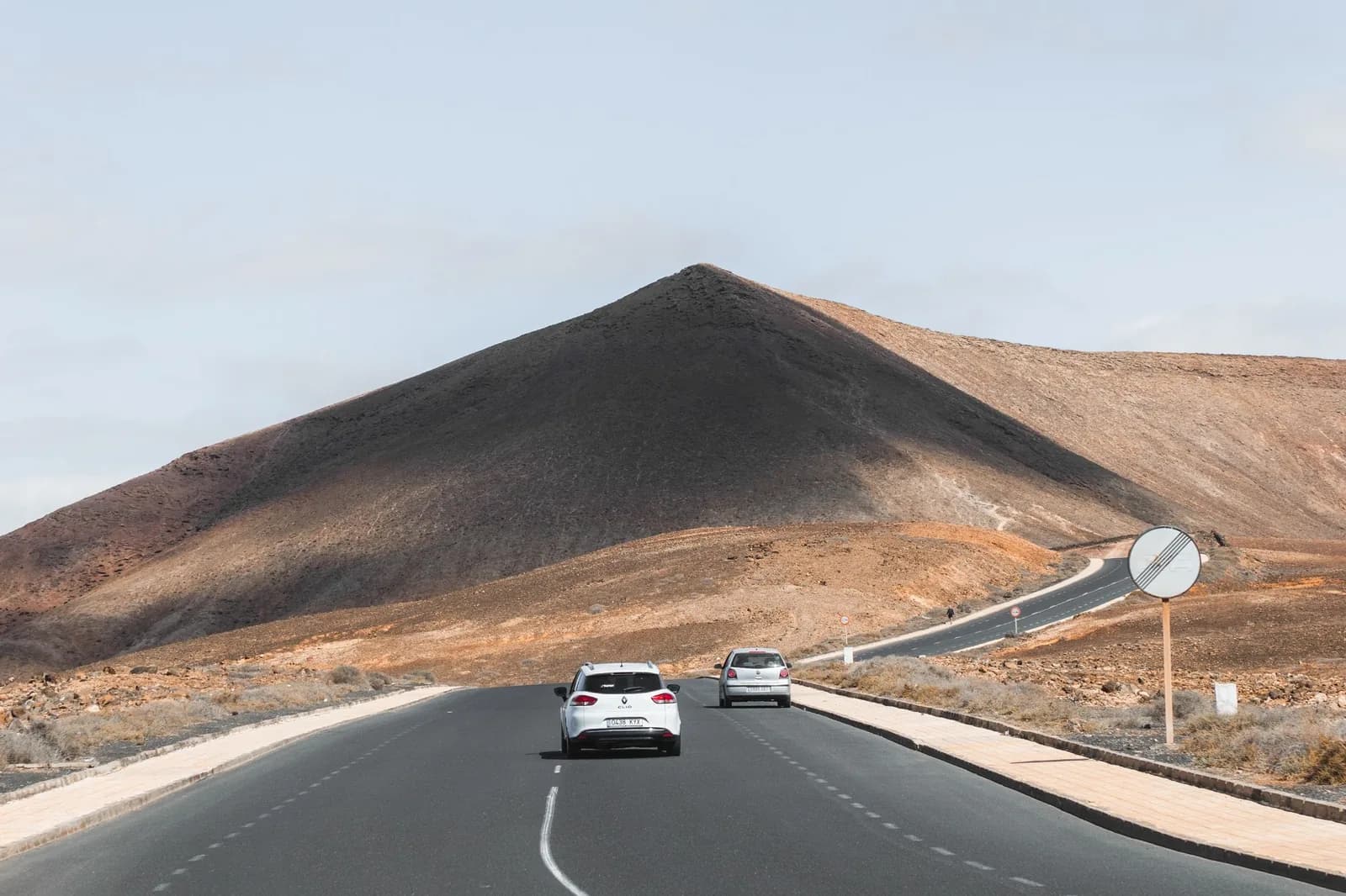 Deux voitures sur une route au pied d'un cône volcanique brun, à Lanzarote