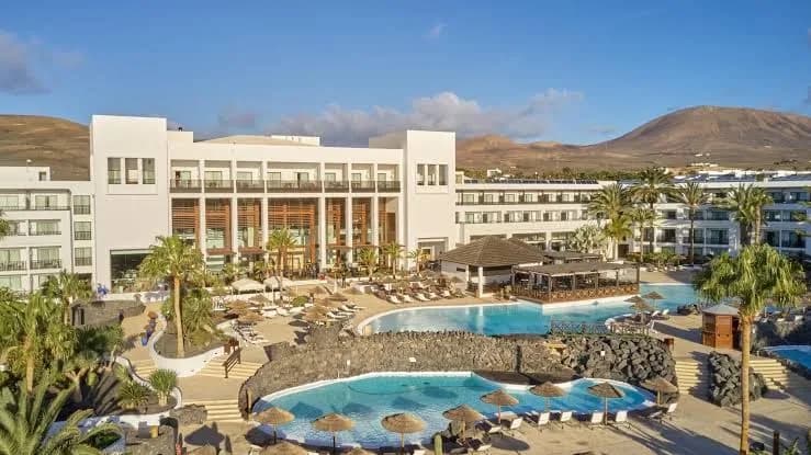 Bâtiment blanc et piscines du Secrets Lanzarote Resort & Spa à Puerto Calero, avec un volcan au fond